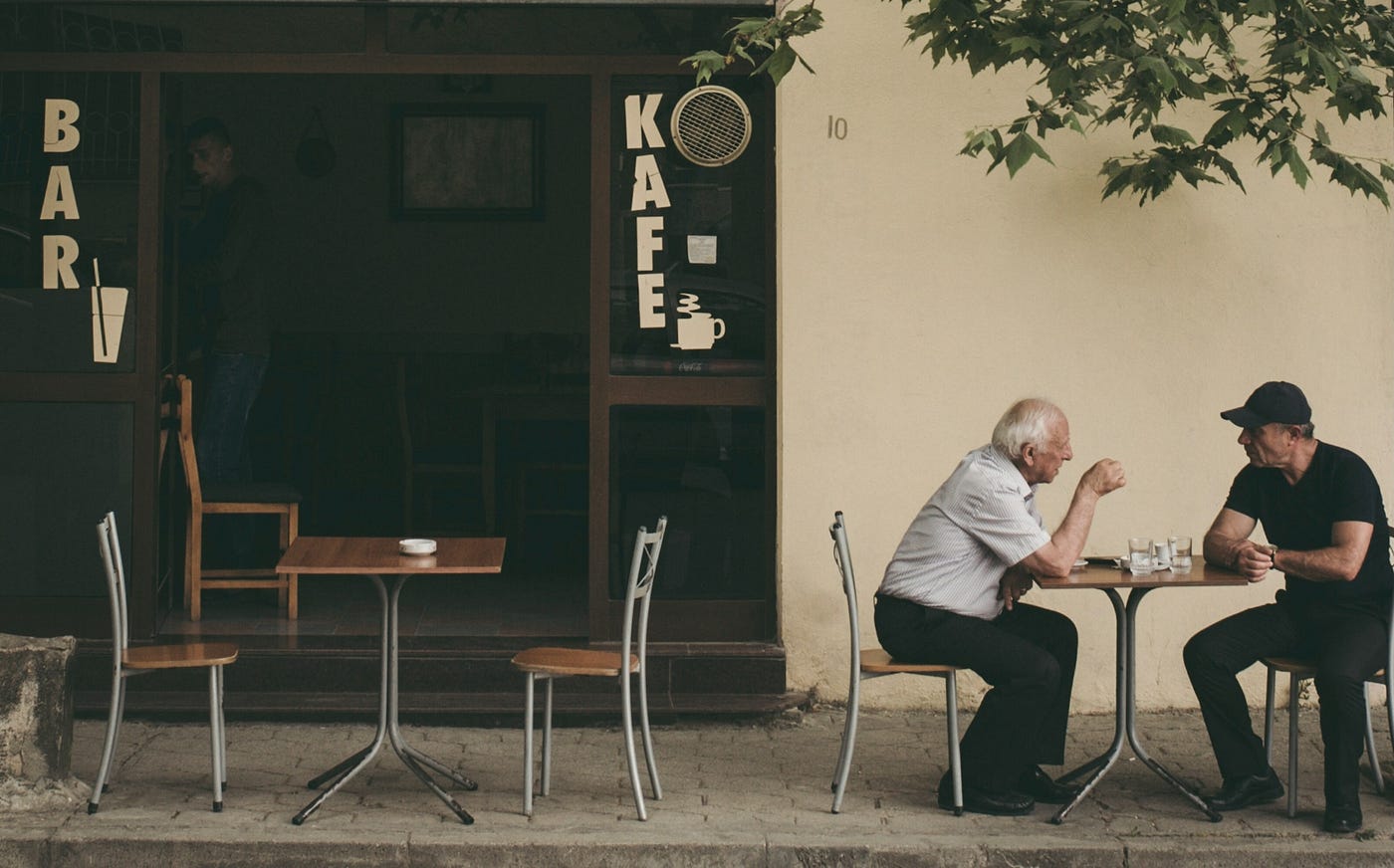 Two old men sit and chat at a table outside a coffee shop in the city of Dürres, Albania.